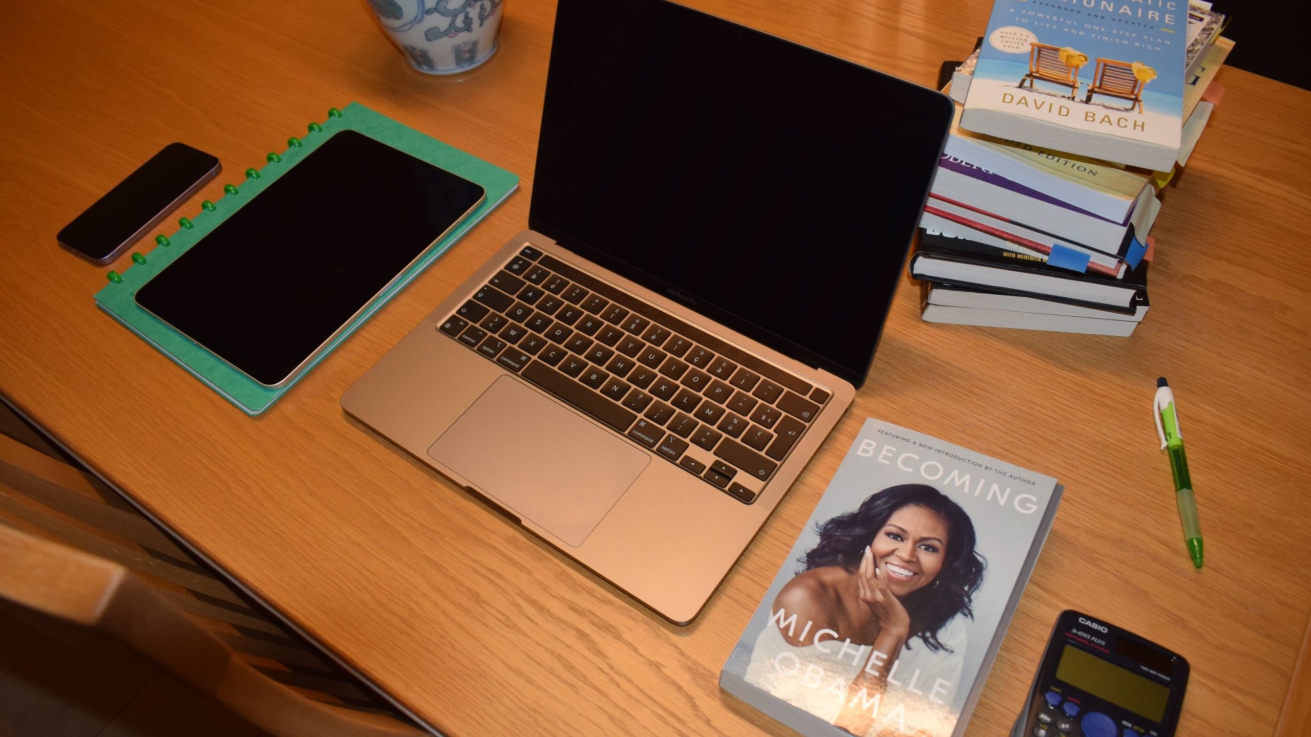 Table de travail avec un ordinateur portable, une tablette, des livres financiers, une calculatrice et le livre 'Becoming' de Michelle Obama – Illustration d'une formation en ligne pour entrepreneurs sur les finances personnelles.