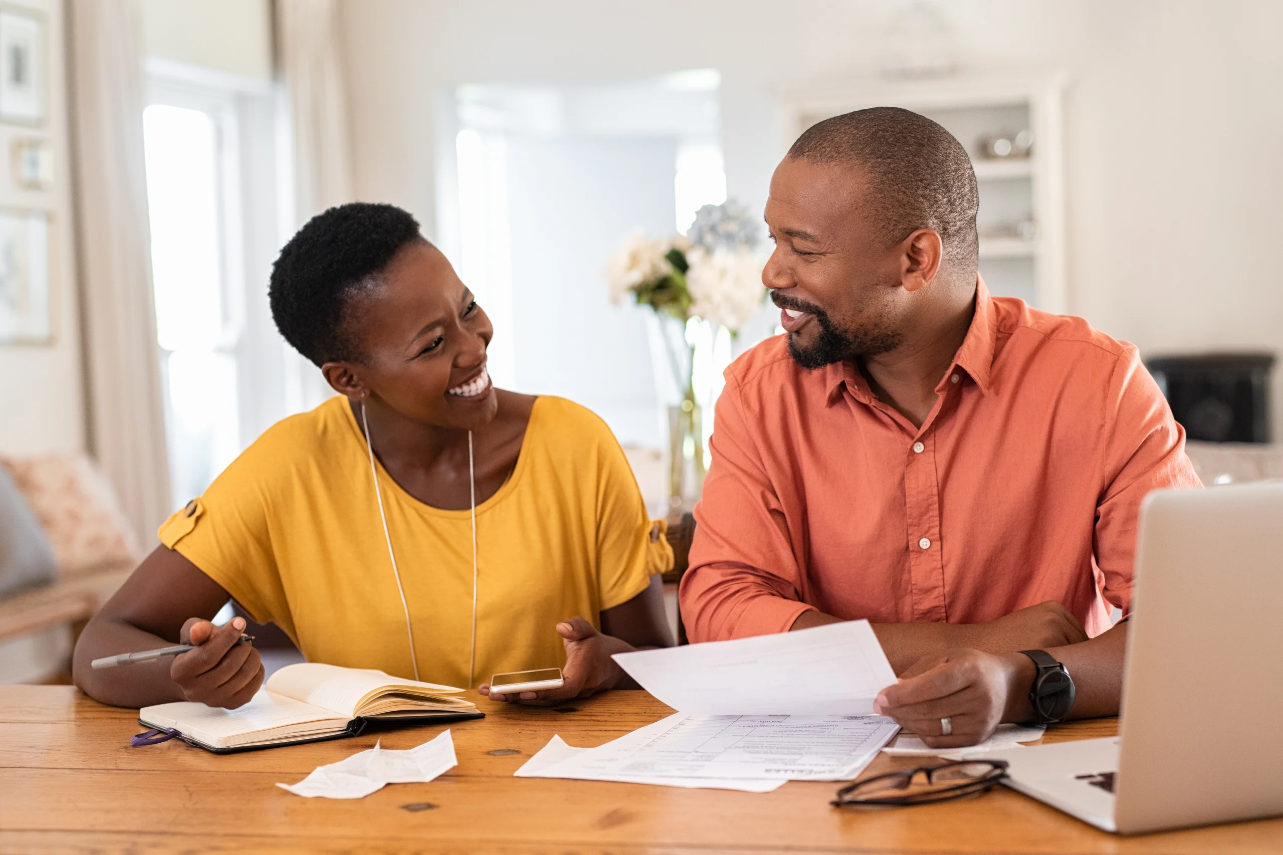 Couple souriant et serein gérant ses finances personnelles avec un carnet et un ordinateur portable.