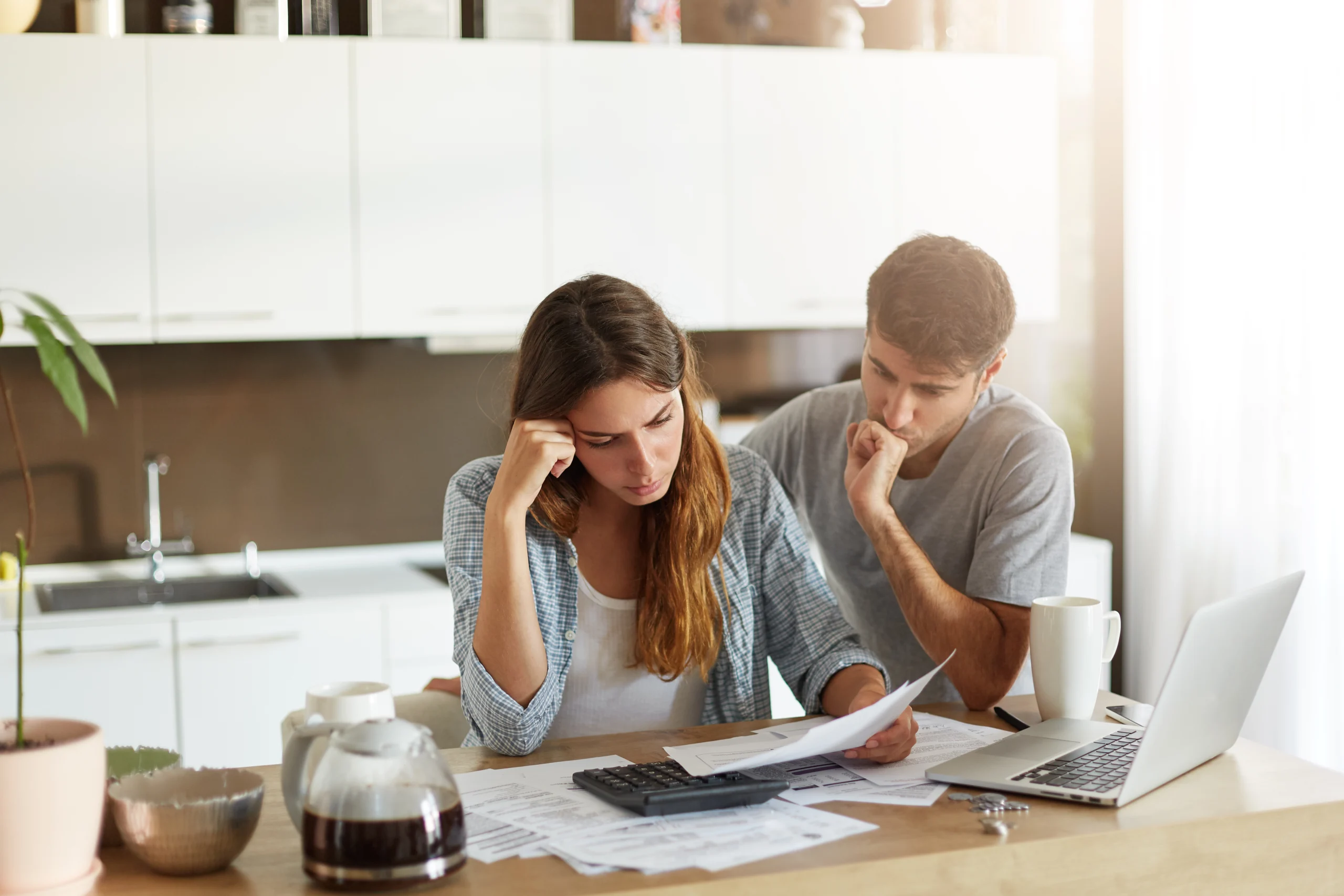 Un couple inquiet consultant des factures avec une calculatrice, illustrant le stress lié à la gestion des finances personnelles.